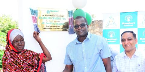 A woman and a man shake hands beside a plaque marking the opening of Bamburi Cement’s solar-powered borehole in Vipingo.