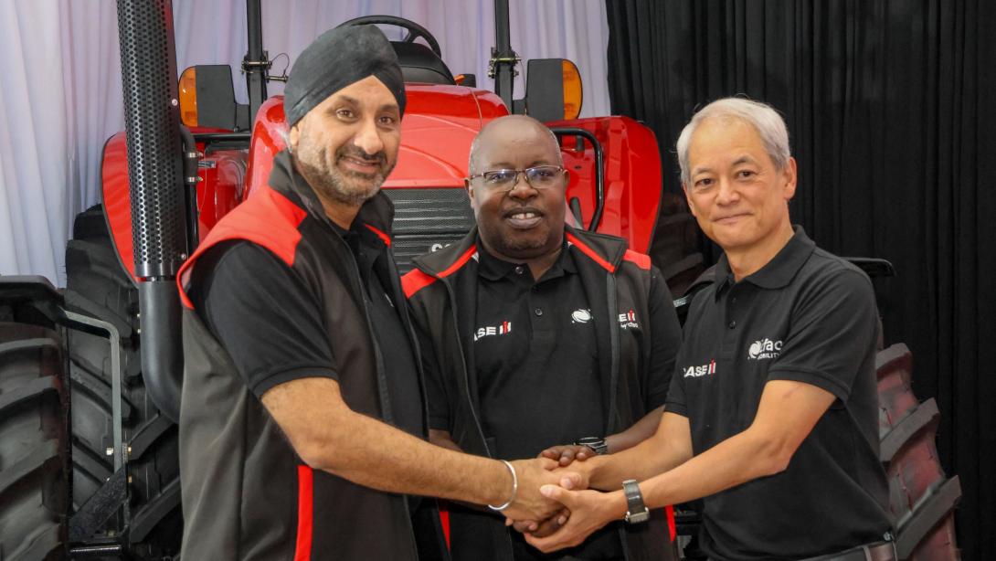 Three men wearing Case IH and CFAO Mobility-branded clothing clasp hands in front of a red tractor.