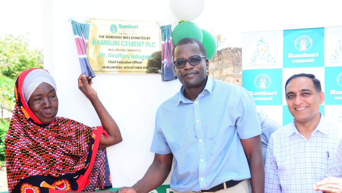 A woman and a man shake hands beside a plaque marking the opening of Bamburi Cement’s solar-powered borehole in Vipingo.
