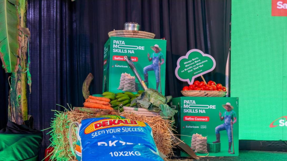 Vegetables, bananas, a seed bag and farming tools are displayed alongside Safire Connect promotional materials at Safaricom’s forum in Githunguri.