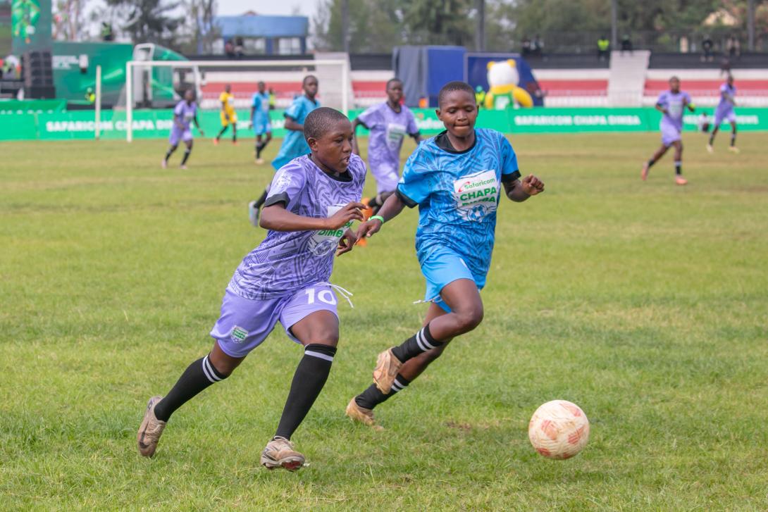 Players in purple and blue kits chase the ball during a Safaricom Chapa Dimba football match.