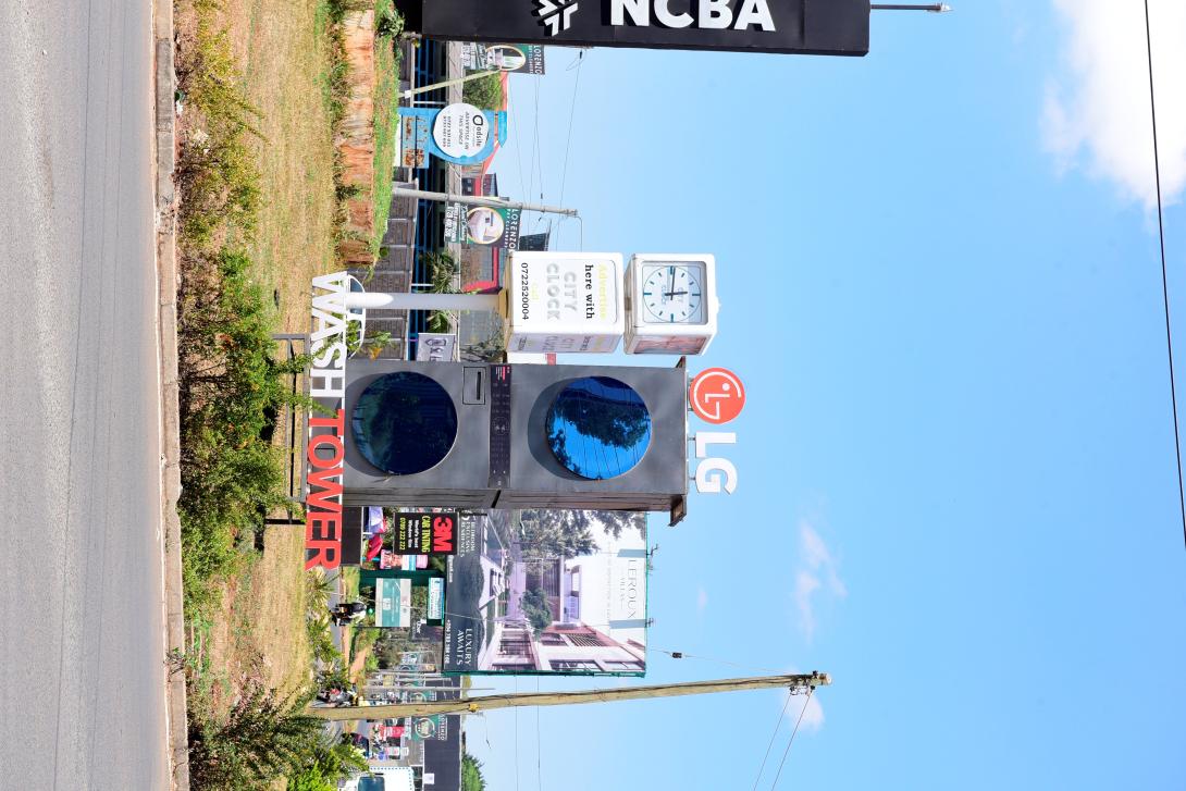 An LG WashTower display stands beside a clock on a landscaped roadside island in Nairobi.