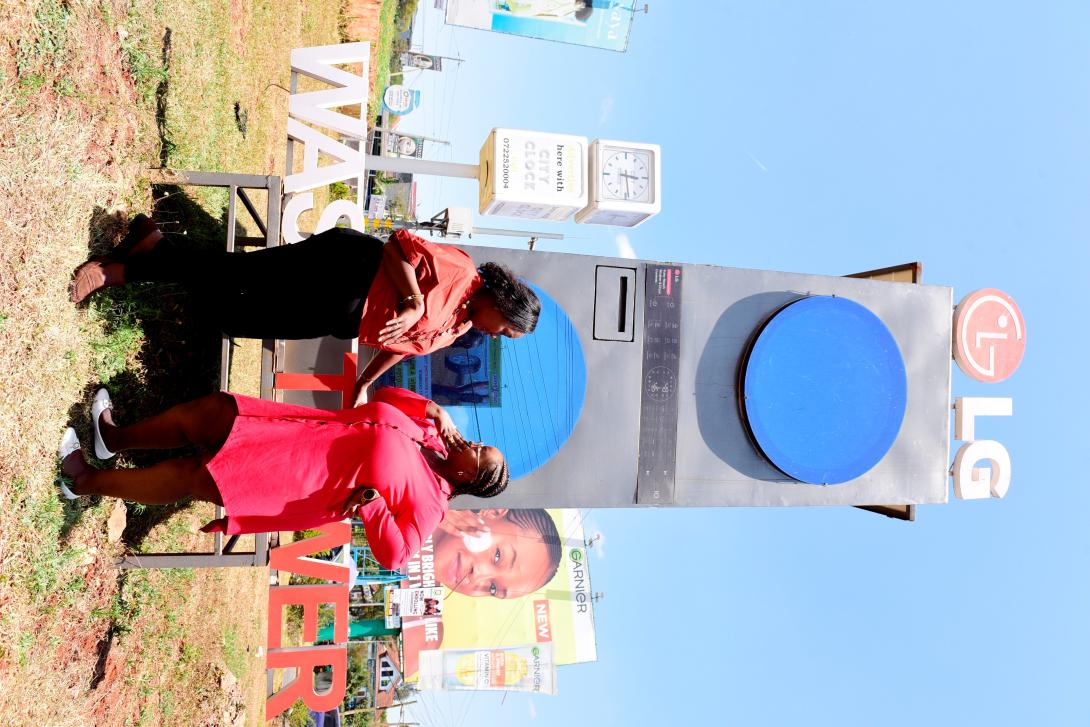 Two women stand beside a large LG WashTower promotional installation at a roadside showcase in Nairobi.
